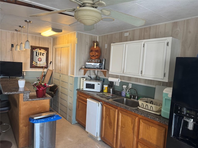 kitchen with sink, black refrigerator with ice dispenser, wood walls, decorative light fixtures, and white cabinets