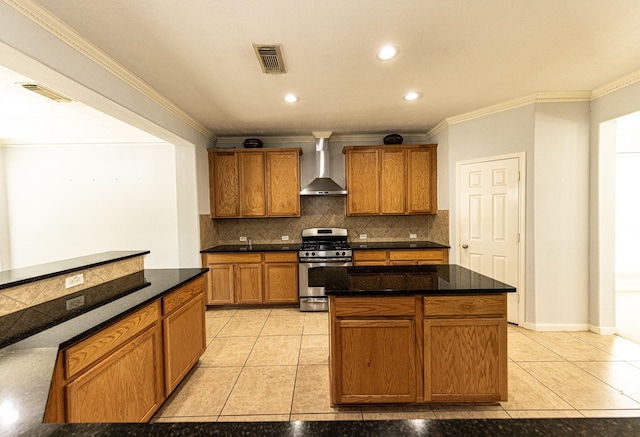 kitchen with light tile patterned flooring, backsplash, wall chimney range hood, stainless steel gas stove, and a kitchen island