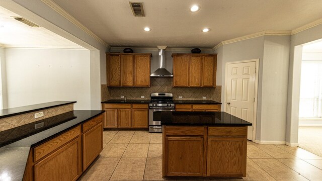 kitchen with stainless steel gas stove, wall chimney exhaust hood, a kitchen island, light tile patterned floors, and ornamental molding