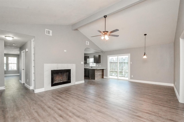 unfurnished living room with high vaulted ceiling, hardwood / wood-style flooring, ceiling fan, a premium fireplace, and beam ceiling