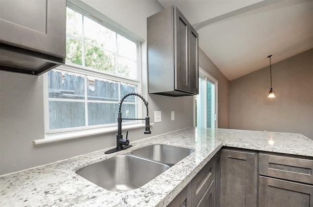 kitchen featuring light stone counters, sink, pendant lighting, and lofted ceiling