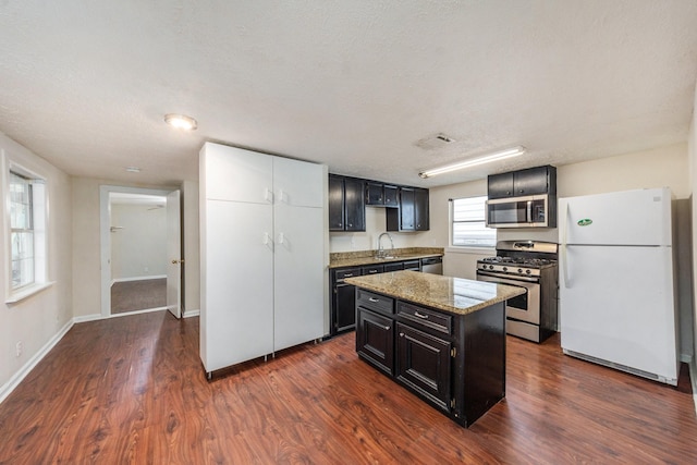 kitchen featuring light stone counters, dark hardwood / wood-style flooring, a textured ceiling, a kitchen island, and appliances with stainless steel finishes