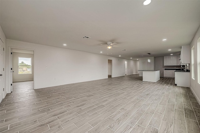 unfurnished living room with light wood-type flooring, ceiling fan, and sink