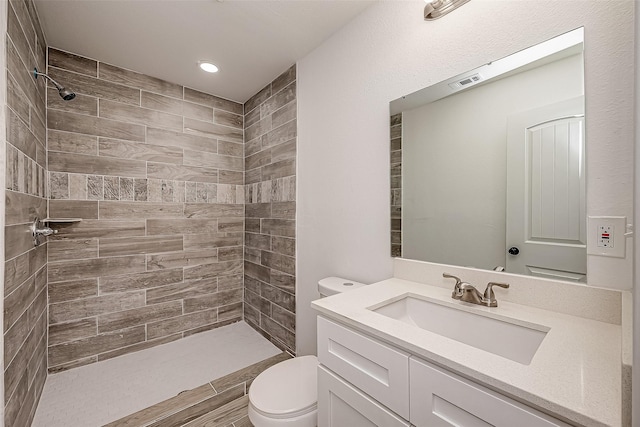 bathroom with tiled shower, vanity, and toilet