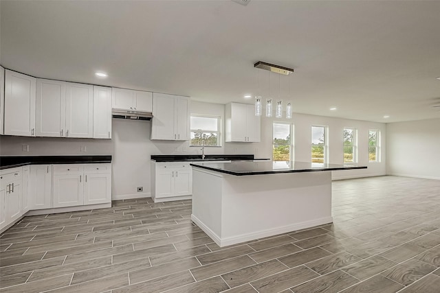 kitchen with white cabinets, decorative light fixtures, a kitchen island, and sink