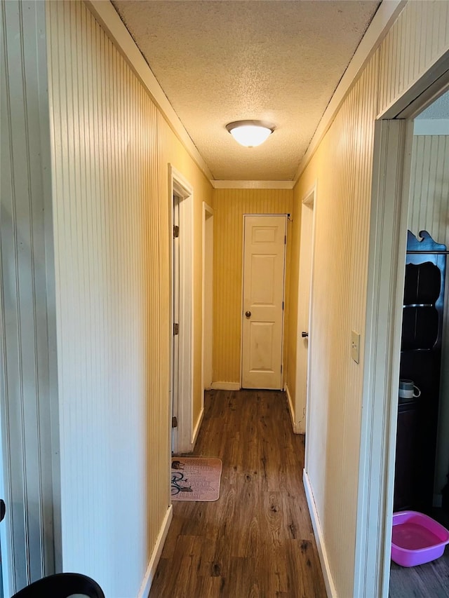 hall featuring crown molding, dark hardwood / wood-style flooring, a textured ceiling, and wooden walls