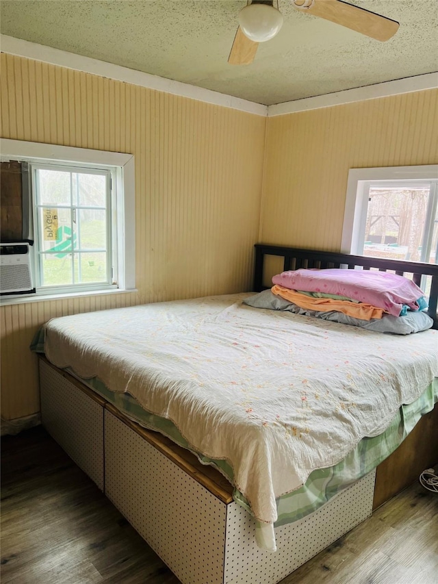 bedroom with ceiling fan, wood walls, and wood finished floors