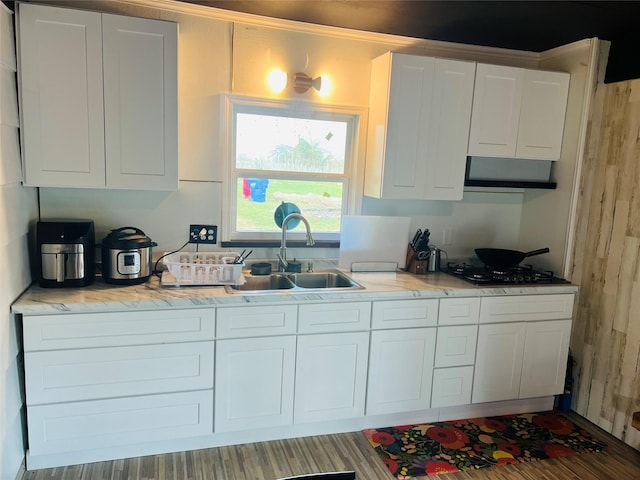 kitchen with gas cooktop, hardwood / wood-style flooring, white cabinetry, and sink