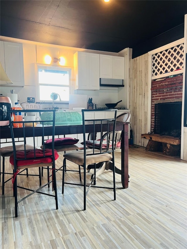 dining area with wood walls, light wood-type flooring, and a brick fireplace