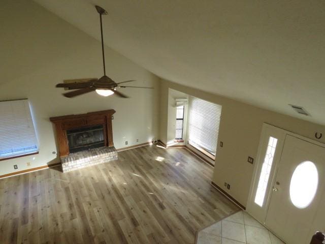 unfurnished living room featuring a wealth of natural light, a fireplace, vaulted ceiling, and light wood-type flooring