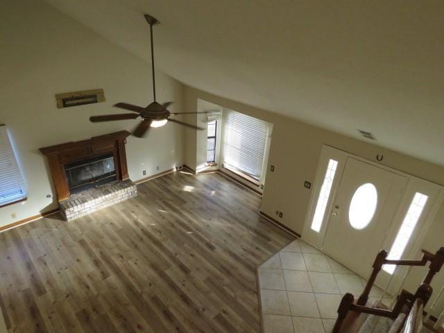 unfurnished living room with a brick fireplace, vaulted ceiling, and ceiling fan