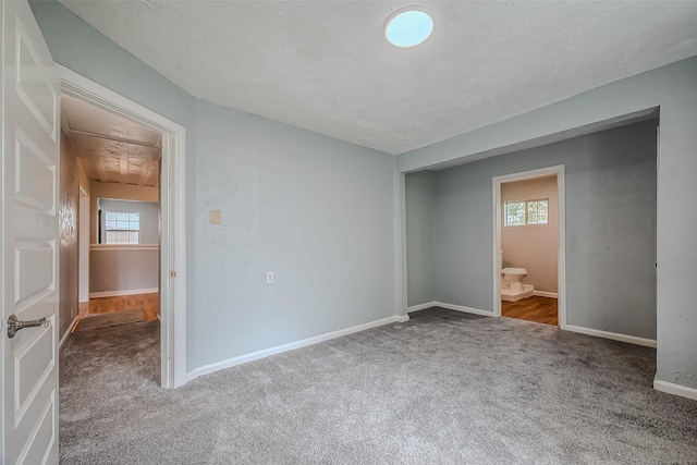 unfurnished bedroom featuring carpet floors, a textured ceiling, and ensuite bath