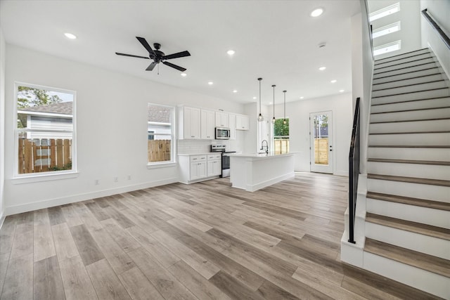 unfurnished living room featuring ceiling fan, sink, and light wood-type flooring