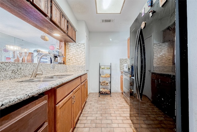 kitchen featuring backsplash, black fridge, electric stove, sink, and light stone counters