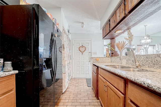 kitchen featuring light stone countertops, sink, a chandelier, a textured ceiling, and black refrigerator