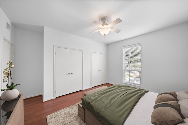 bedroom featuring dark hardwood / wood-style flooring, ceiling fan, and multiple closets