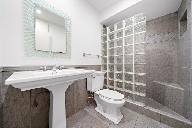 bathroom featuring tile patterned floors, tiled shower, toilet, and tile walls