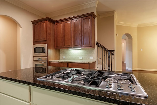 kitchen with appliances with stainless steel finishes, dark stone counters, ornamental molding, and backsplash