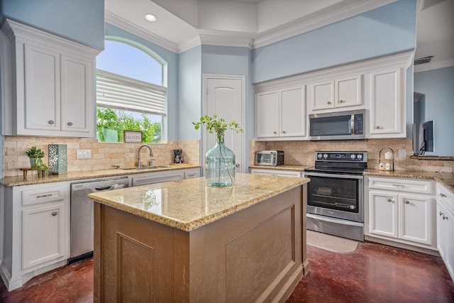 kitchen with white cabinets, sink, light stone countertops, appliances with stainless steel finishes, and a kitchen island