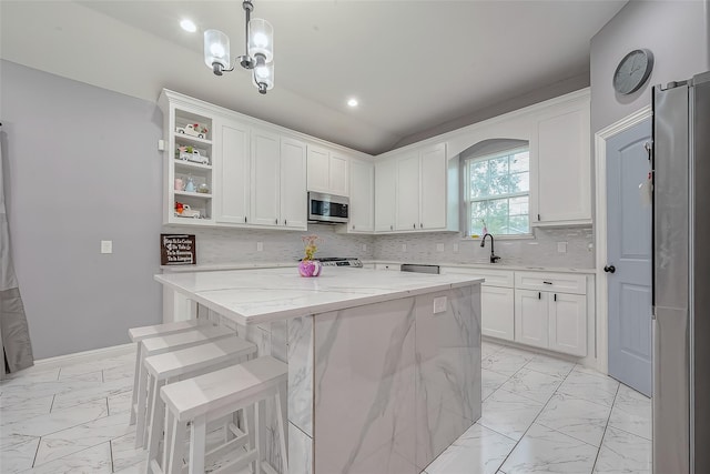 kitchen with appliances with stainless steel finishes, light stone counters, decorative light fixtures, white cabinets, and a kitchen island