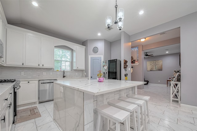 kitchen with white cabinets, appliances with stainless steel finishes, a kitchen island, and light stone countertops