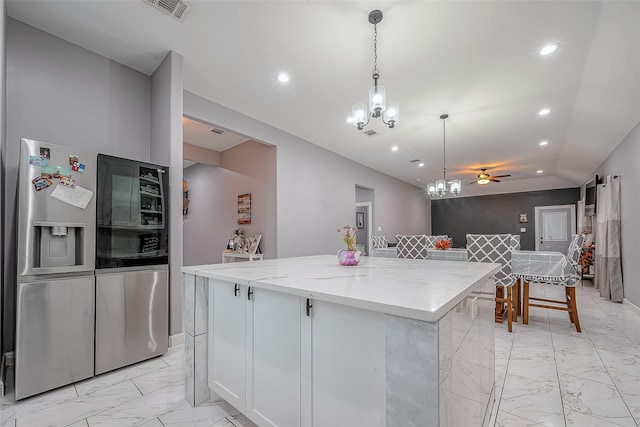 kitchen with light stone counters, white cabinets, stainless steel fridge with ice dispenser, a center island, and hanging light fixtures