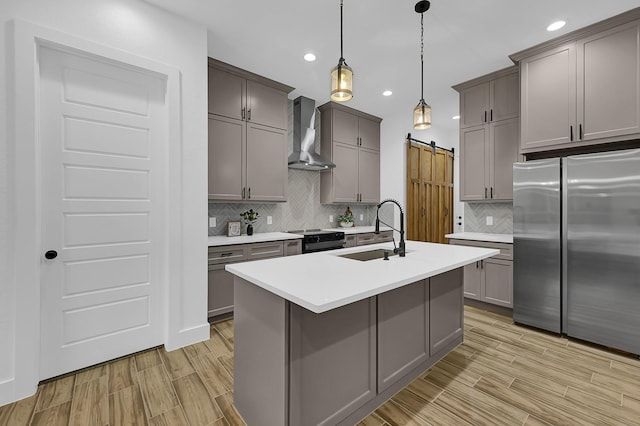 kitchen featuring wall chimney range hood, sink, black electric range, stainless steel fridge, and a barn door