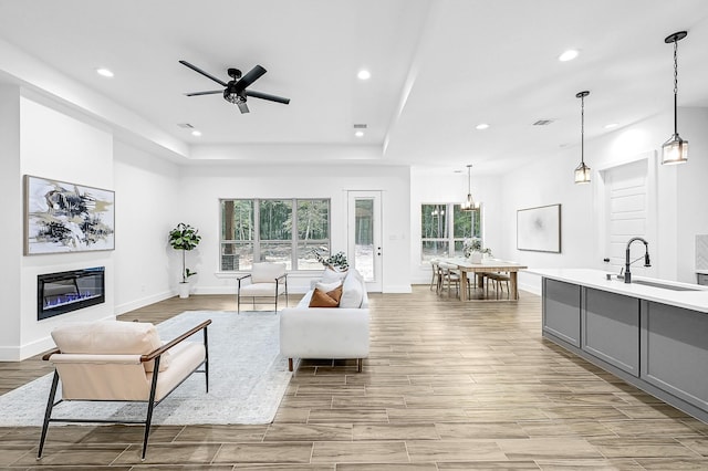 living room featuring a tray ceiling, ceiling fan, sink, and plenty of natural light