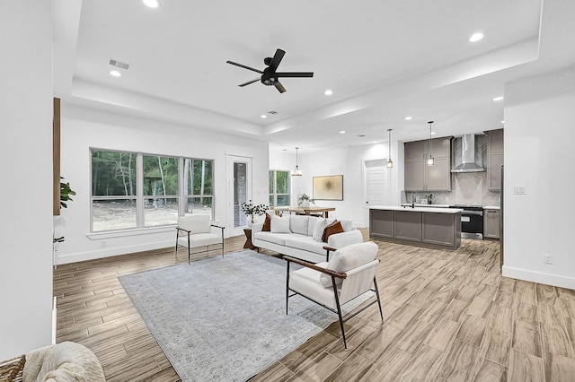 living room featuring ceiling fan, a raised ceiling, and sink