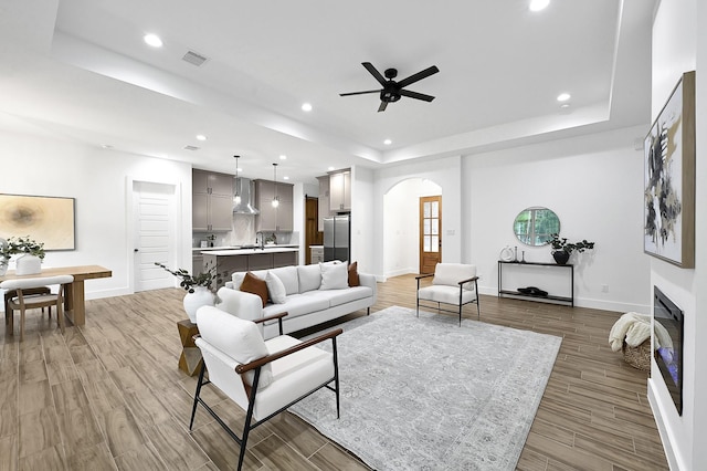 living room featuring ceiling fan, light wood-type flooring, and a tray ceiling