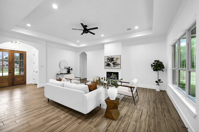 living room featuring a raised ceiling, ceiling fan, french doors, and plenty of natural light