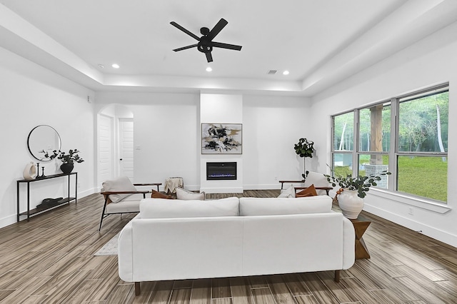 living room with wood-type flooring, a tray ceiling, and ceiling fan