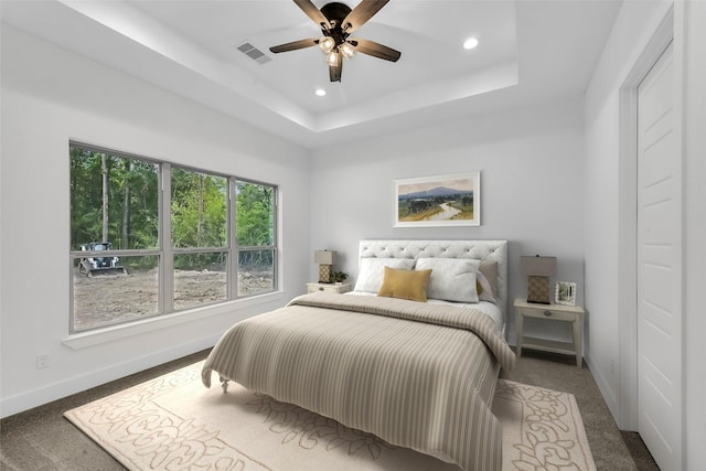 carpeted bedroom featuring a raised ceiling and ceiling fan