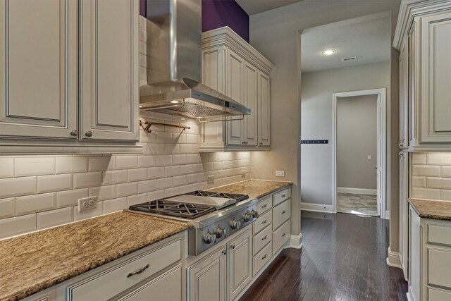 kitchen with tasteful backsplash, light stone counters, dark hardwood / wood-style flooring, stainless steel gas stovetop, and wall chimney range hood