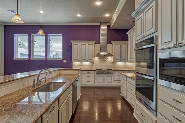 kitchen featuring sink, decorative light fixtures, ornamental molding, stainless steel appliances, and wall chimney range hood