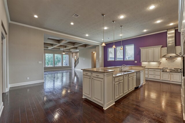 kitchen with decorative light fixtures, coffered ceiling, light stone countertops, a center island with sink, and wall chimney exhaust hood