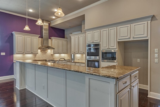 kitchen with dark wood finished floors, wall chimney exhaust hood, cream cabinets, stainless steel appliances, and backsplash