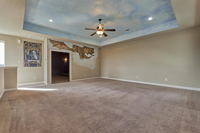 unfurnished living room with a tray ceiling, carpet flooring, and baseboards