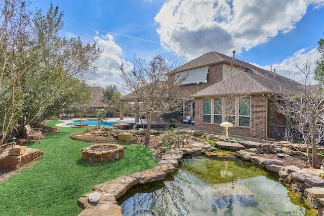 back of property with brick siding, a shingled roof, a lawn, fence, and an outdoor pool