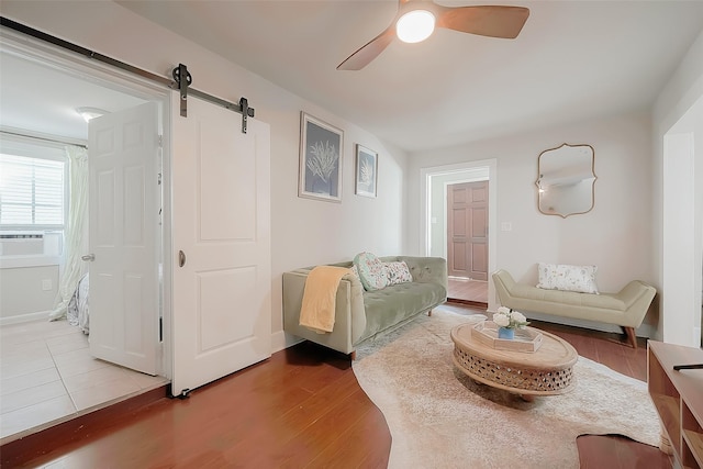 living room with wood-type flooring, a barn door, and ceiling fan