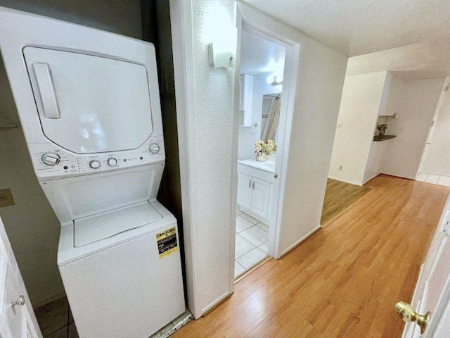 laundry area featuring a textured ceiling, stacked washer / dryer, and light hardwood / wood-style flooring