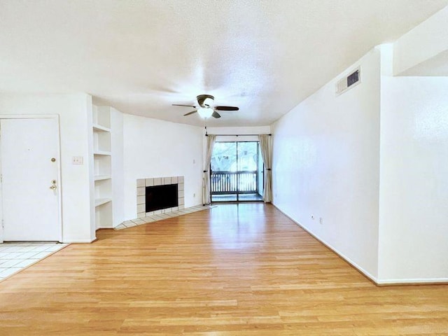 unfurnished living room with a tile fireplace, ceiling fan, built in features, light hardwood / wood-style flooring, and a textured ceiling