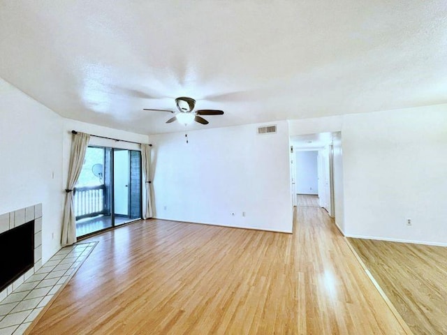 unfurnished living room with a tiled fireplace, ceiling fan, light hardwood / wood-style floors, and a textured ceiling