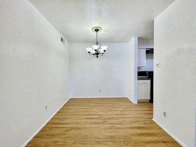 empty room with light hardwood / wood-style floors, a textured ceiling, and a chandelier