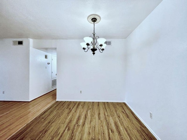 empty room with hardwood / wood-style floors, a notable chandelier, and a textured ceiling