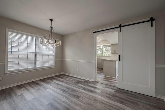 unfurnished dining area with a notable chandelier, a barn door, light wood-type flooring, and a healthy amount of sunlight