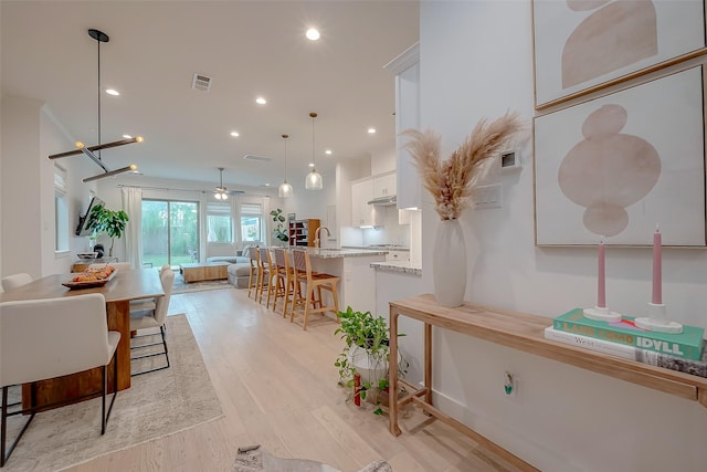 kitchen featuring light stone countertops, light wood-type flooring, a breakfast bar, decorative light fixtures, and white cabinets