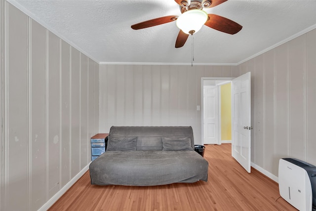 living area with ceiling fan, hardwood / wood-style floors, a textured ceiling, and ornamental molding