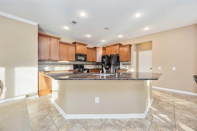 kitchen featuring sink, dark stone countertops, an island with sink, light tile patterned floors, and black appliances