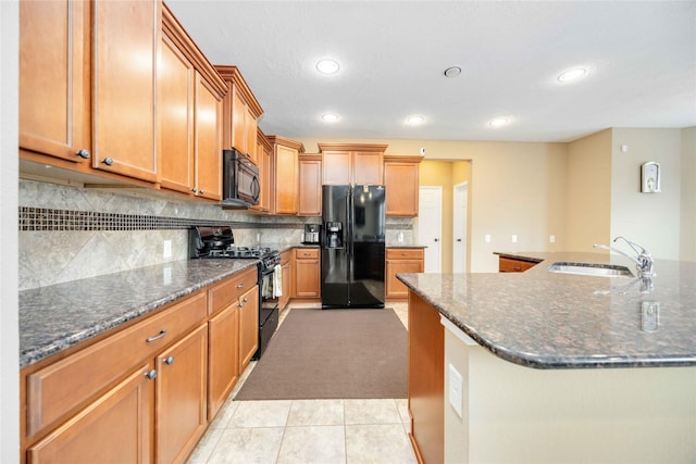 kitchen featuring sink, tasteful backsplash, dark stone counters, light tile patterned flooring, and black appliances